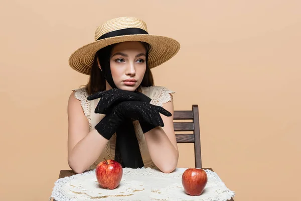 Pretty model in sun hat and gloves looking away near apples isolated on beige — Fotografia de Stock