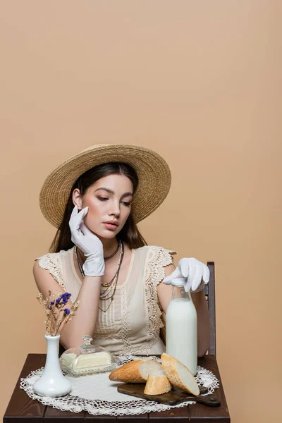 Trendy model in sun hat touching bottle of milk near butter and bread isolated on beige — Fotografia de Stock