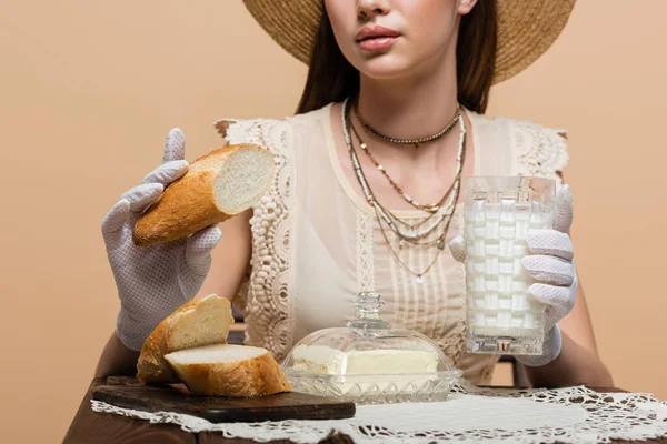 Обрізаний вид молодої жінки в рукавичках, що тримає хліб і молоко біля масла ізольовані на бежевому — стокове фото