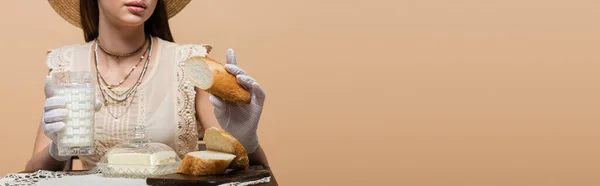 Cropped view of woman in gloves holding milk and bread near butter isolated on beige, banner — Stock Photo