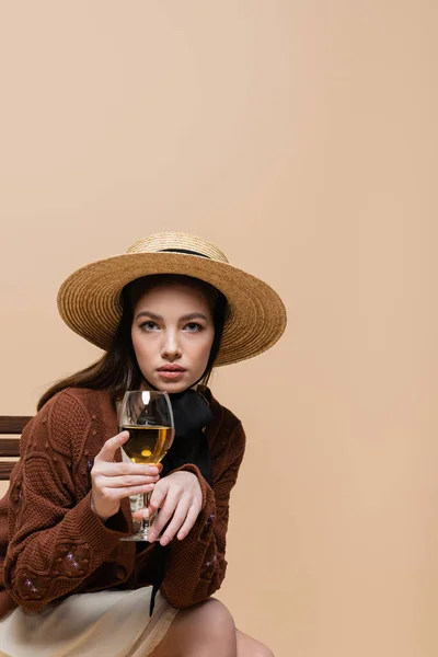 Модна жінка тримає келих вина і дивиться на камеру ізольовано на бежевому — стокове фото