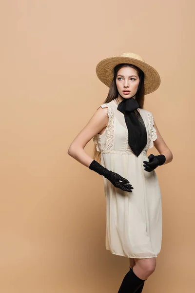 Модна молода жінка в вінтажному платті і сонячний капелюх позує ізольовано на бежевому — стокове фото