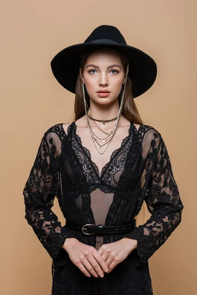 Portrait of brunette woman in hat and guipure robe looking at camera isolated on beige — Stockfoto