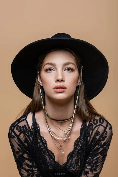 Portrait of trendy brunette woman in black hat looking at camera isolated on beige — Photo de stock