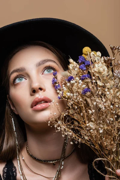 Portrait of stylish woman in black fedora hat looking away near plants isolated on beige — Foto stock