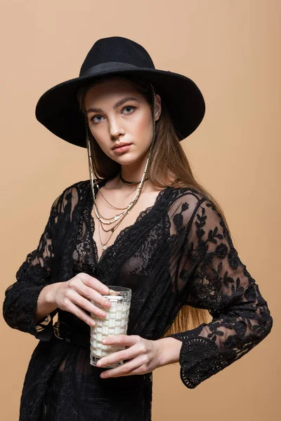 Stylish woman in fedora hat holding glass of milk isolated on beige — Stock Photo