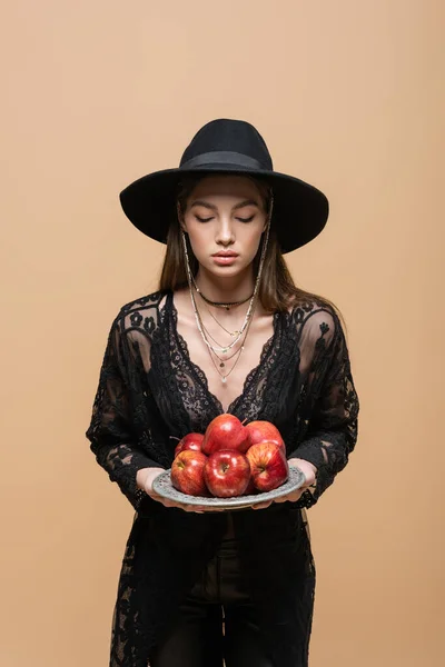 Trendy young woman in fedora hat holding fresh apples isolated on beige — Stock Photo