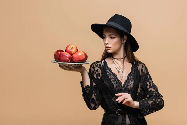 Fashionable young woman holding plate with ripe apples isolated on beige - foto de stock