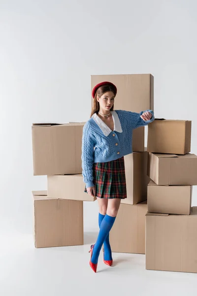 Full length of trendy model standing near carton boxes on white background — Stockfoto