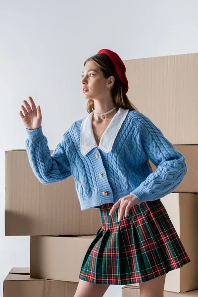 Pretty brunette woman in skirt and knitted cardigan posing near carton boxes isolated on grey — Foto stock
