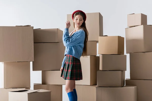 Модна молода жінка в береті і в'язаний кардиган дивиться далеко біля картонних коробок ізольовані на сірому — стокове фото