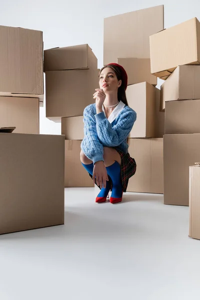 Trendy model in knitted cardigan posing near cardboard boxes on white background - foto de stock