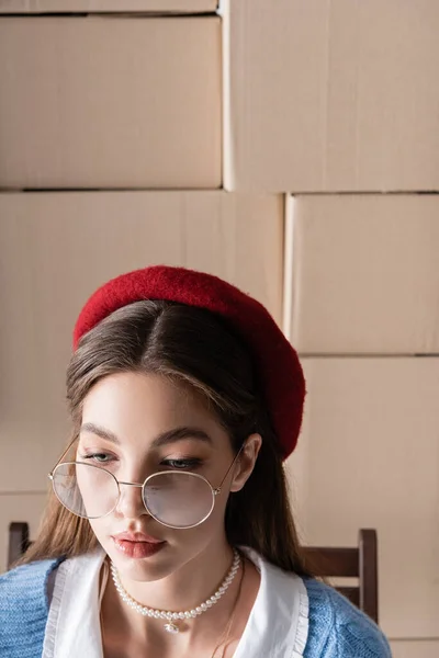 Portrait of brunette woman in eyeglasses and beret near cardboard boxes at background — Stock Photo