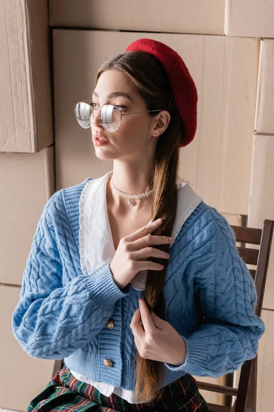 Stylish woman in beret and eyeglasses touching hair near cardboard boxes — Stockfoto