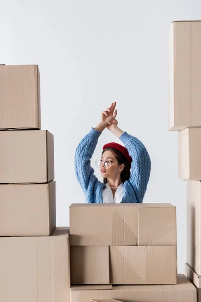 Brunette woman in eyeglasses and knitted cardigan posing behind near cardboard boxes isolated on white — Foto stock