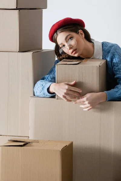 Trendy young woman in eyeglasses hugging cardboard box isolated on white — Stock Photo