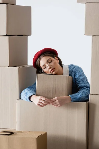 Fashionable woman in beret and eyeglasses standing near cardboard boxes isolated on white — Foto stock