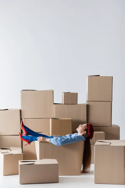 Side view of woman in heels and eyeglasses sitting in cardboard box on white background — Photo de stock