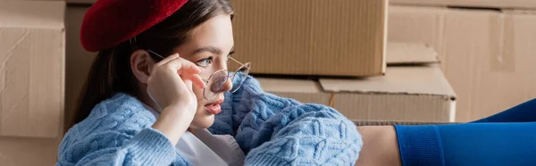 Stylish woman in eyeglasses looking away near cardboard boxes, banner — Stock Photo