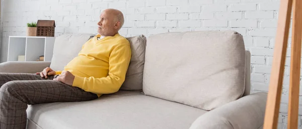 Side view of pensioner sitting on couch at home, banner — Stockfoto