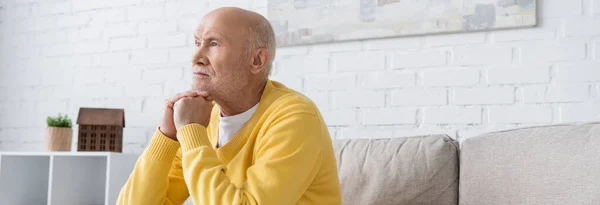 Старший мужчина смотрит в сторону, сидя на диване дома, баннер — стоковое фото