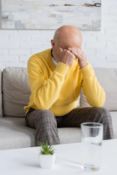 Upset pensioner sitting on couch in living room - foto de stock