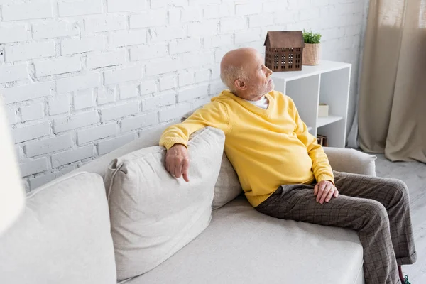 Вид сбоку пожилого человека, сидящего дома на диване — стоковое фото