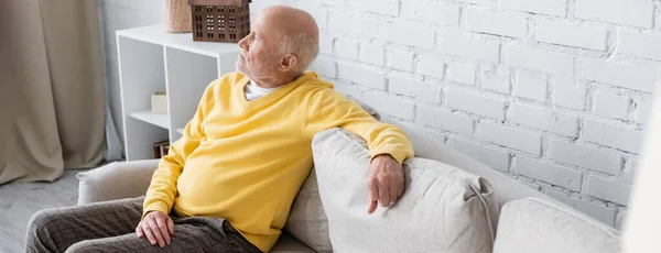 Side view of grey haired man sitting on couch in living room, banner — Stockfoto