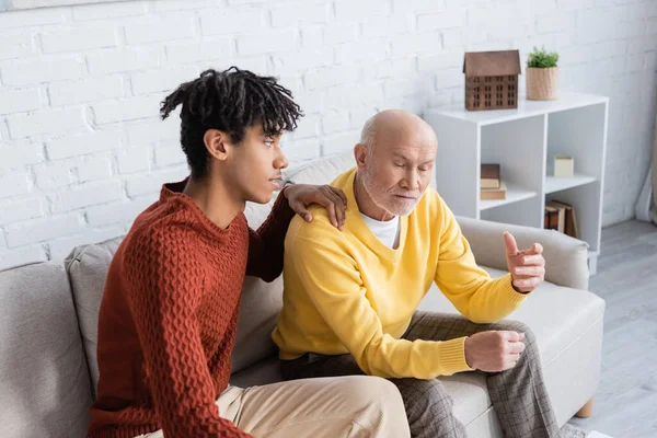 African american grandson touching elderly grandpa in living room — Photo de stock