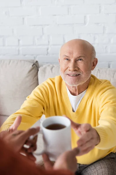 Smiling granddad looking at blurred african american grandson with cup of tea at home — Stockfoto