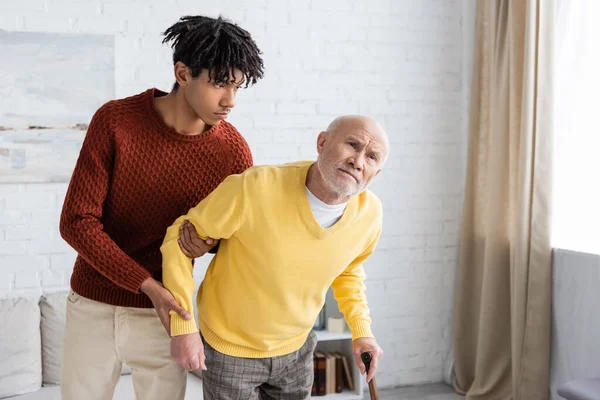 African american grandson supporting grandparent with walking cane at home — Stock Photo