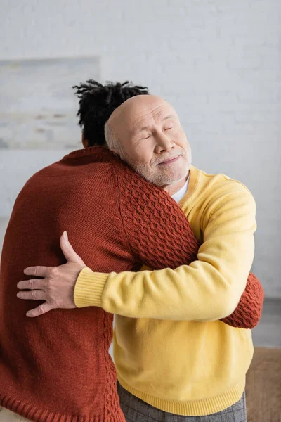 Pensioner embracing african american grandson at home - foto de stock