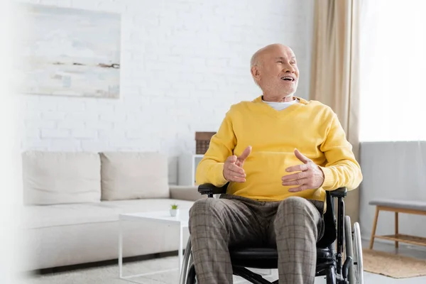 Позитивный пожилой человек смотрит в сторону, сидя в инвалидной коляске дома — стоковое фото