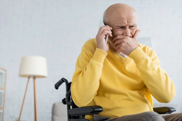 Підсилювач старший чоловік говорить по смартфону, сидячи в інвалідному візку вдома — стокове фото
