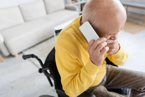 High angle view of displeased pensioner talking on smartphone in wheelchair at home — Stockfoto