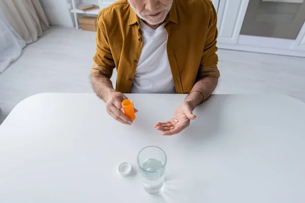 Cropped view of elderly man holding pills near glass of water in kitchen — Stockfoto