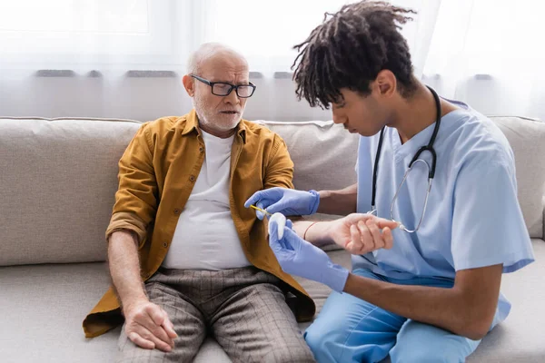 African american nurse doing injection to senior man on couch at home — Stock Photo