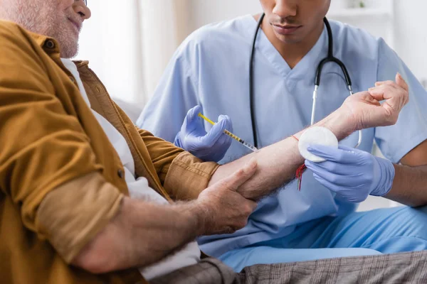 Cropped view of african american nurse doing injection to elderly man at home - foto de stock