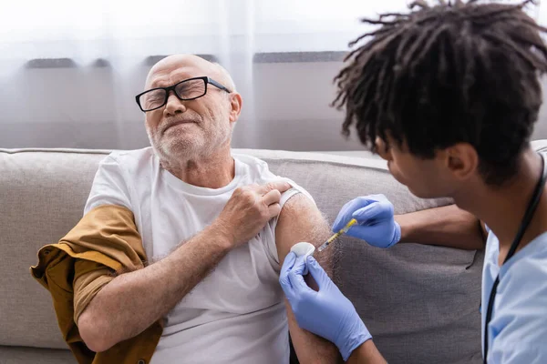 Старший мужчина чувствует боль, в то время как африканская американская медсестра делает инъекции дома — стоковое фото