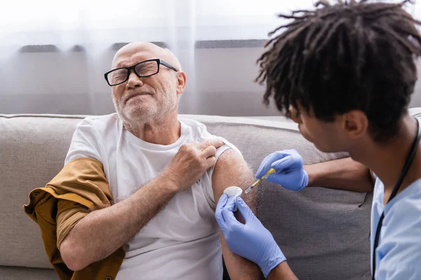 Senior man feeling pain while african american nurse doing injection at home — Stock Photo