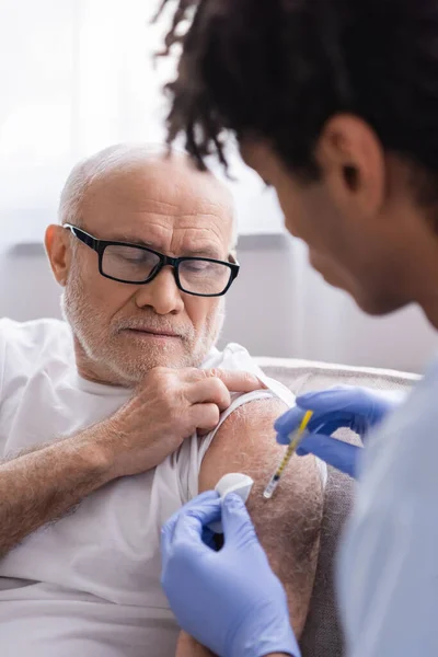 African american nurse holding cotton pad and doing injection to elderly patient at home — Stock Photo
