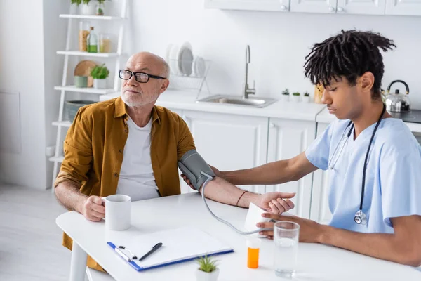 African american nurse checking blood pressure of elderly patient at home — Stock Photo