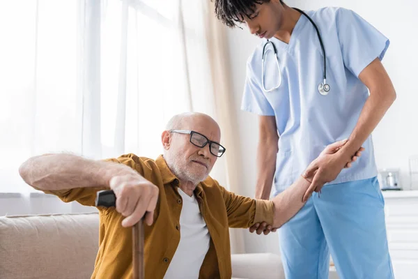 African american nurse helping to elderly patient with walking cane at home — Stock Photo
