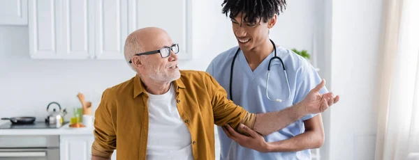 Positive pensioner talking to african american nurse at home, banner - foto de stock