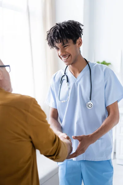 Smiling african american nurse shaking hand of elderly patient at home — Photo de stock