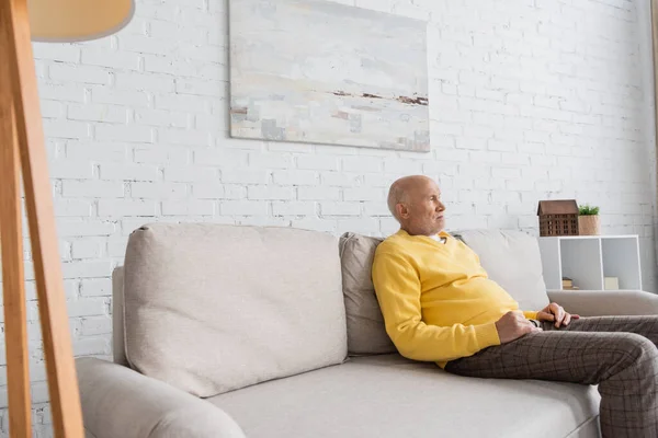 Displeased senior man looking away while sitting on couch at home — Photo de stock