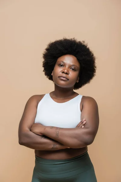 Curly african american plus size woman in crop top standing with crossed arms isolated on beige — Photo de stock