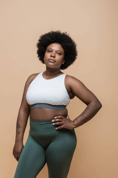 Curly african american plus size woman in crop top standing with hand on hip isolated on beige — Fotografia de Stock