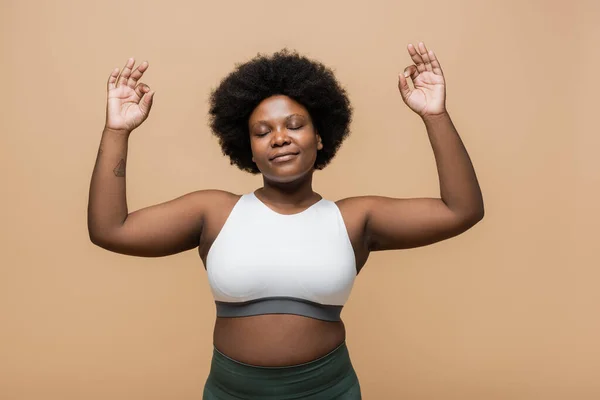 Pleased and curly african american plus size woman in crop top gesturing isolated on beige — Photo de stock