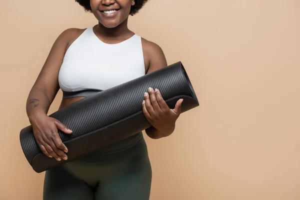 Cropped view of happy african american plus size woman with tattoo holding fitness mat isolated on beige — Stock Photo